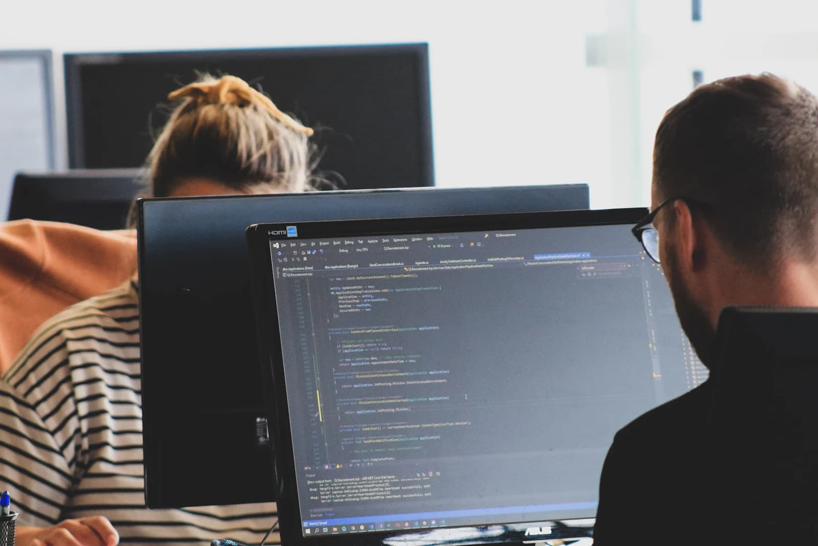 Two developers working on code at their monitors in an open office