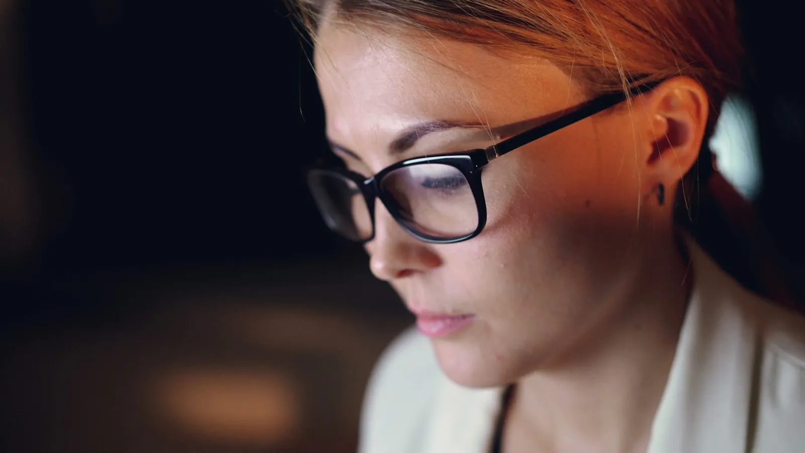 An engineer in glasses studying a screen in a dark room