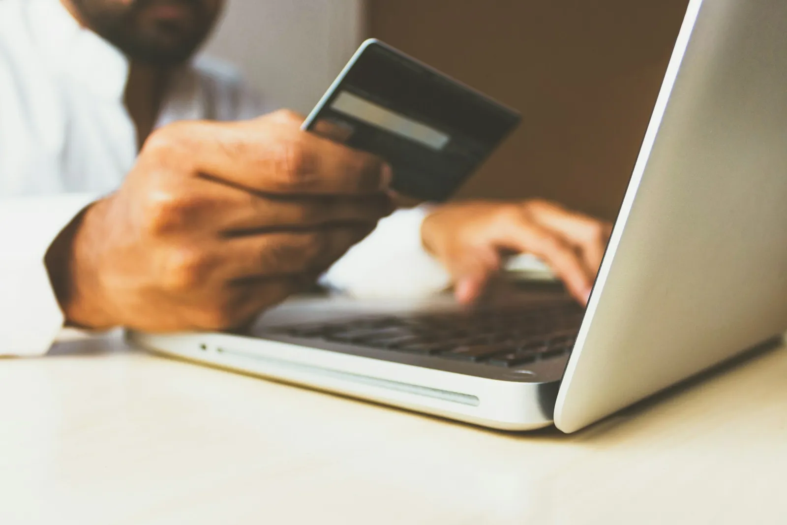 A person holding a payment card while working on a laptop