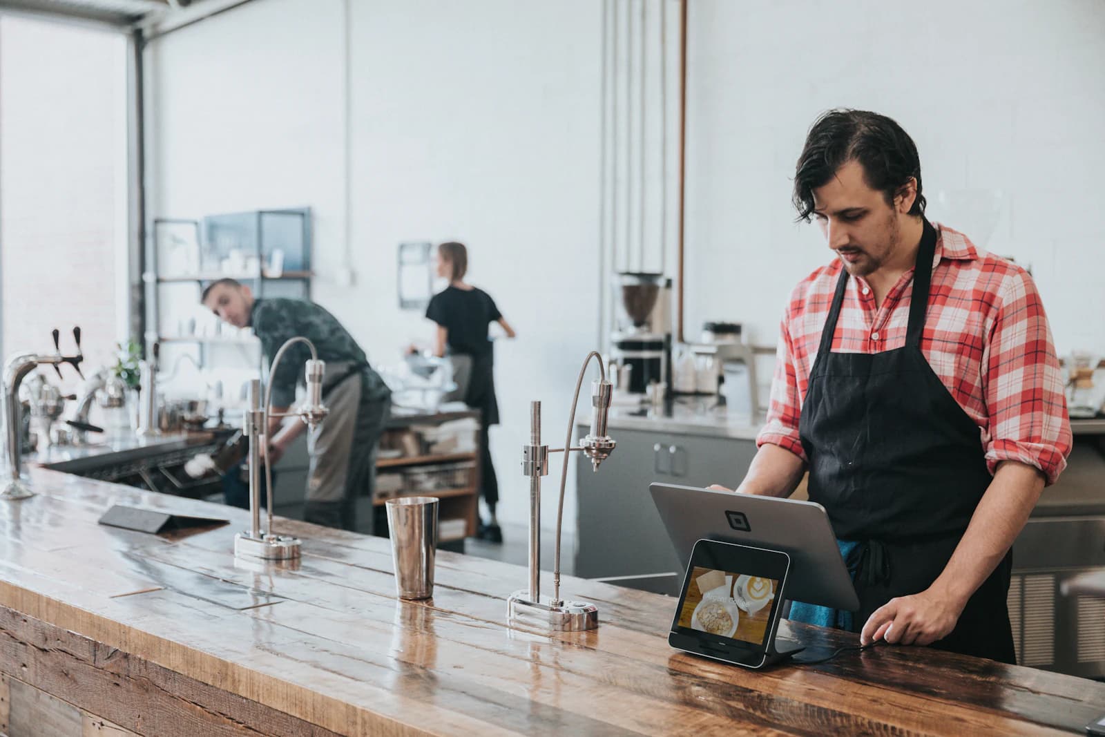 A cafe owner in an apron using a tablet at a wooden counter