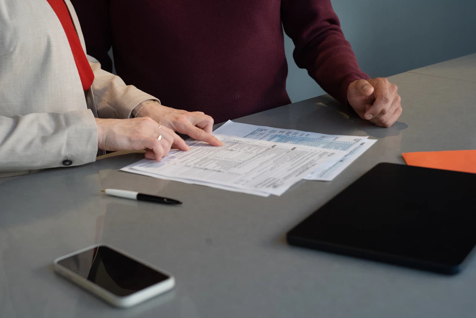 Two colleagues reviewing forms and a tablet at a desk