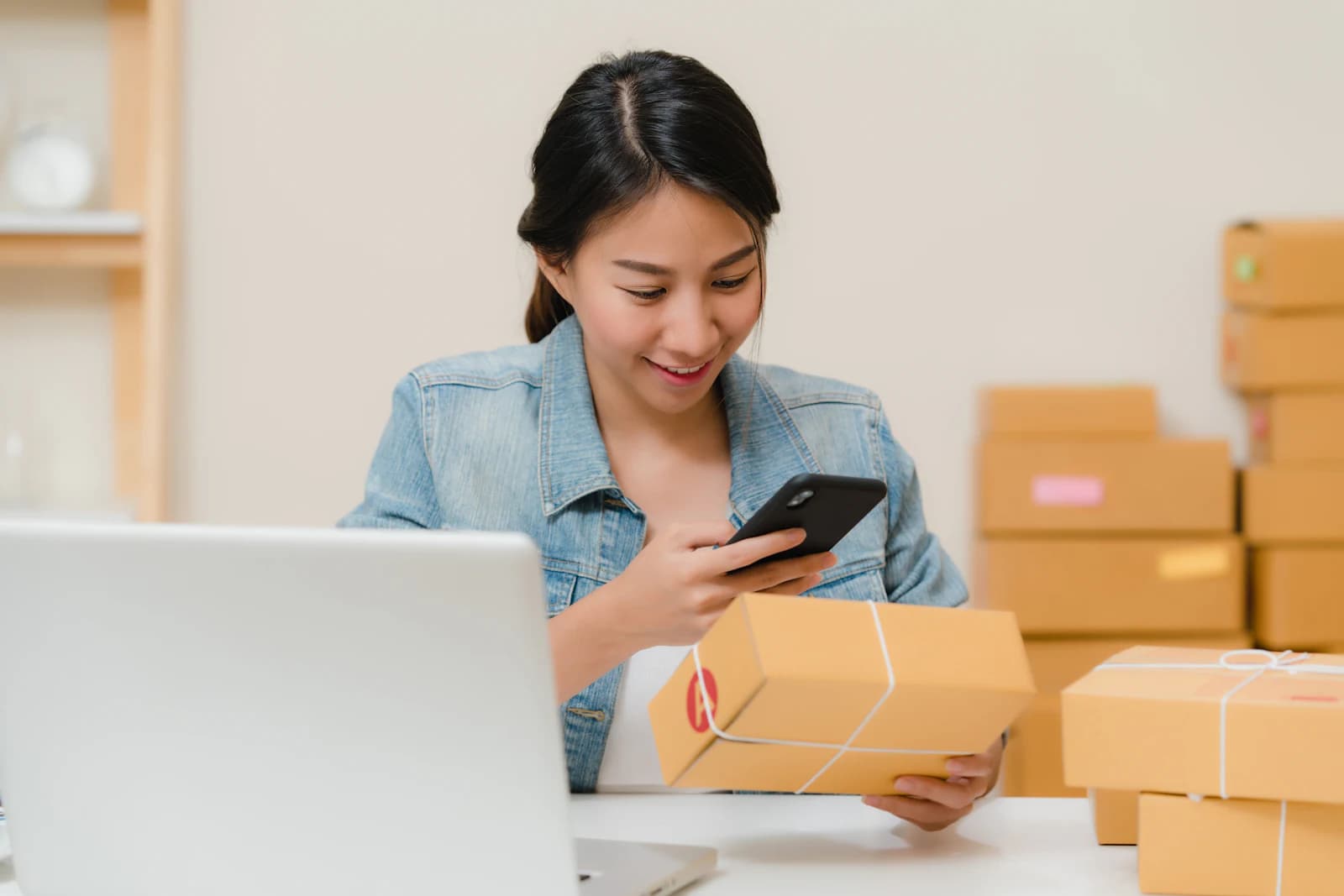 A shop owner checking an order on a phone beside packed parcels