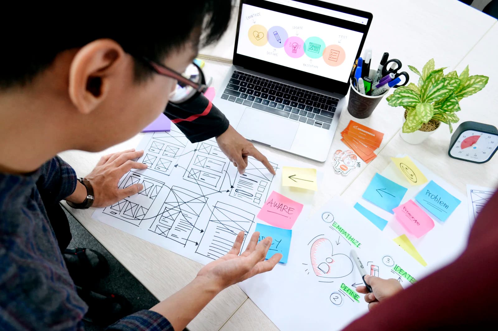 A designer laying out wireframes with sticky notes beside a laptop