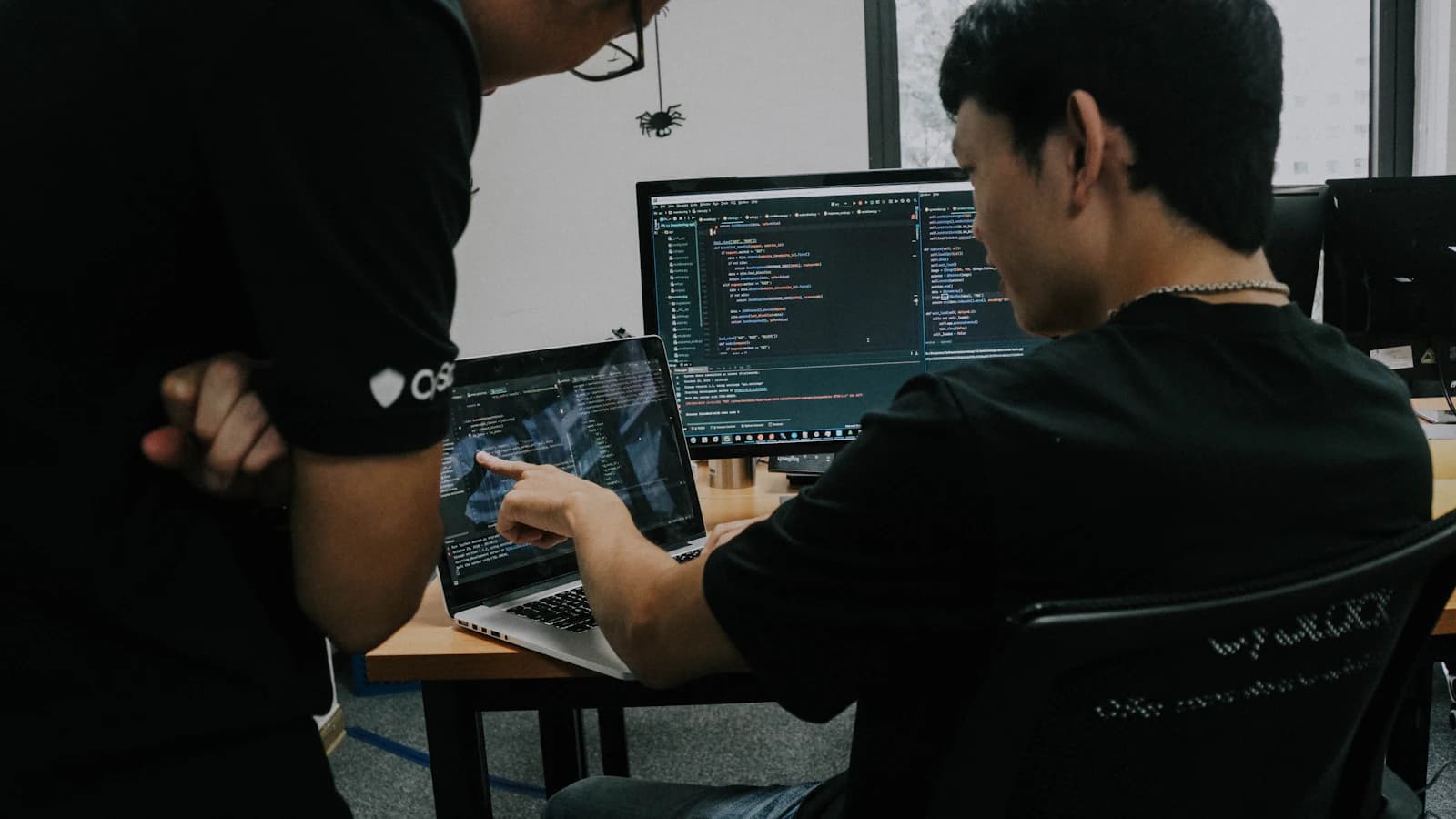 Two engineers reviewing code on a laptop and a monitor