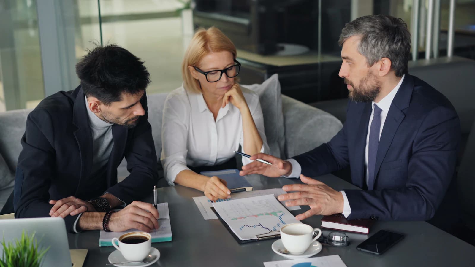Three executives reviewing a printed analysis over coffee
