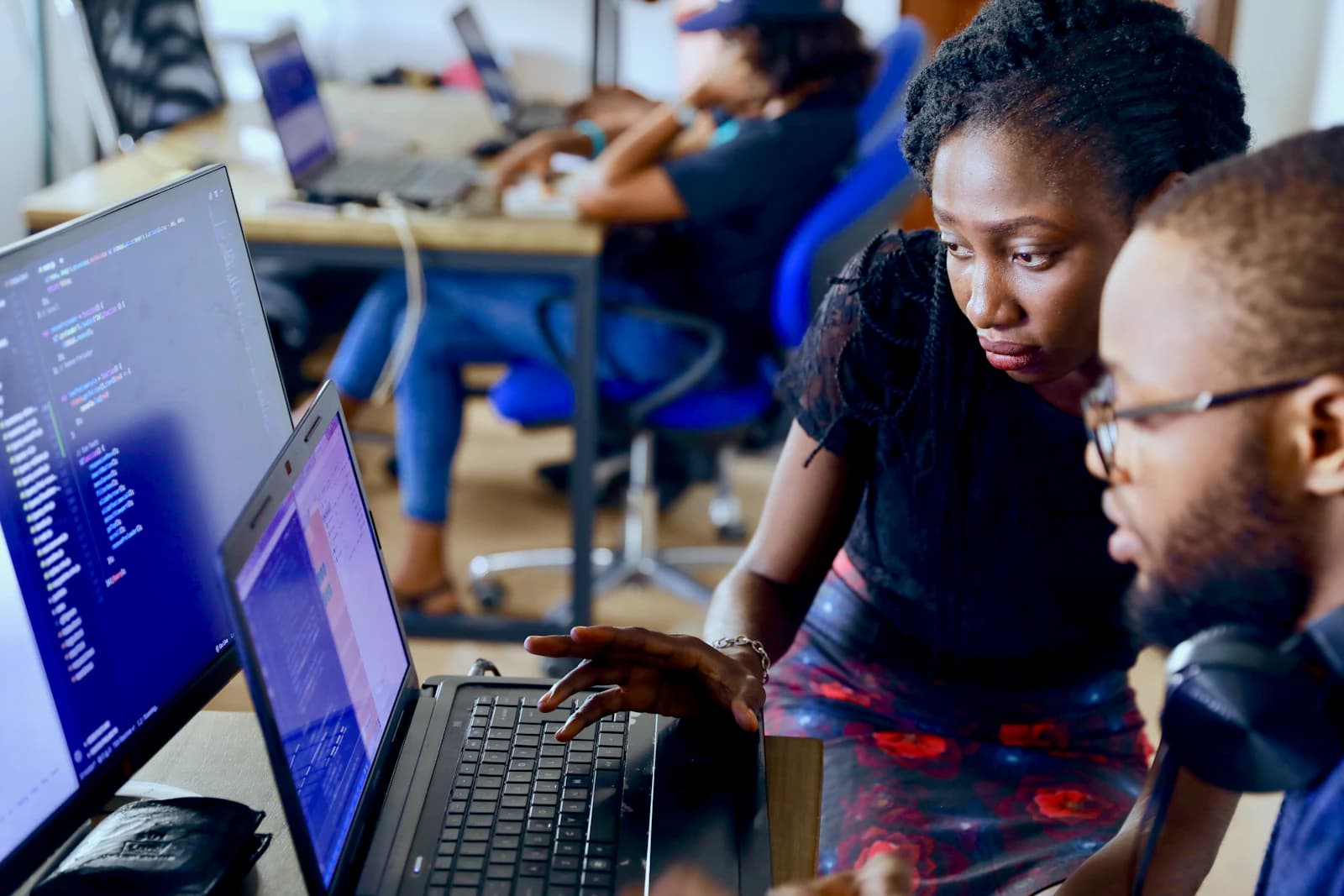 Two engineers reviewing code together on a laptop in a busy office