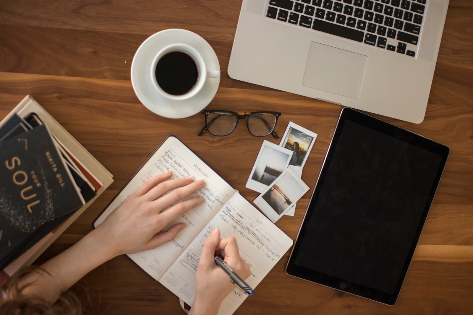 Hands writing notes beside a laptop and a coffee